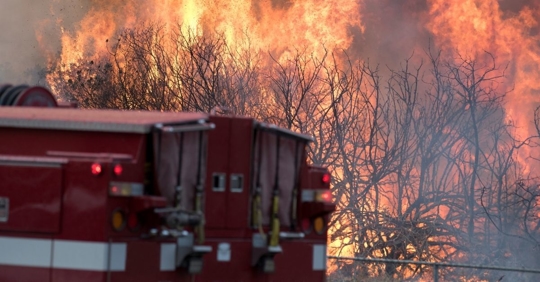 Firetruck in front of a wildfire of burning woods.